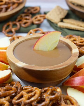 A bowl of caramel dip in the center od a serving tray with sliced apples and pretzels.