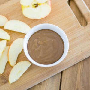 A small bowl of caramel dip with sliced apples on a cutting board.
