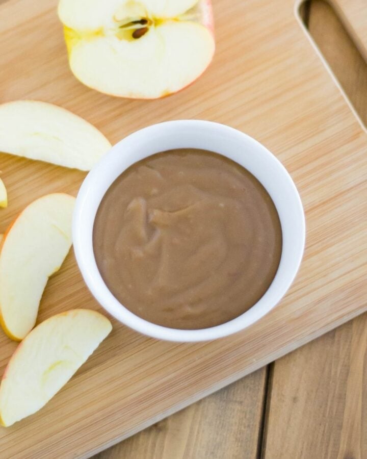 A small bowl of caramel dip with sliced apples on a cutting board.