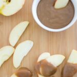 Apple slices dipped in caramel with a bowl in background filled with caramel dip.