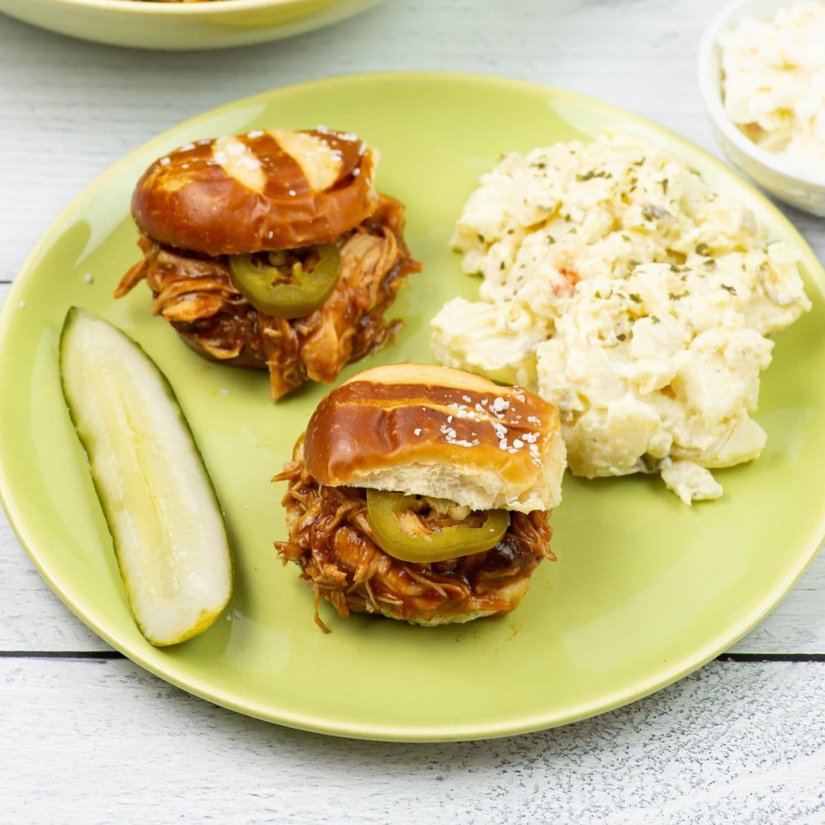 BBQ Cranberry Chicken Sliders served with potato salad, cole slaw and a pickle wedge on a dinner plate.