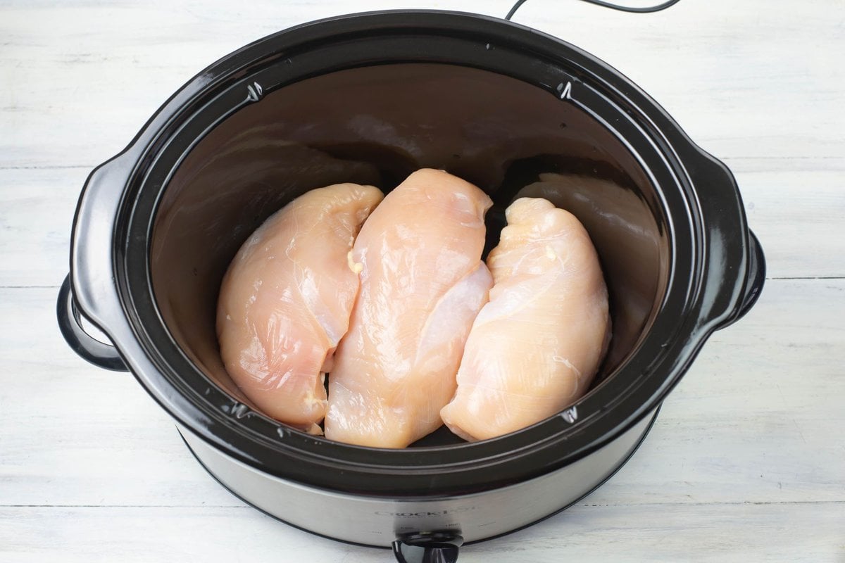 Arranging boneless chicken in the bottom of a 6 quart crock pot.