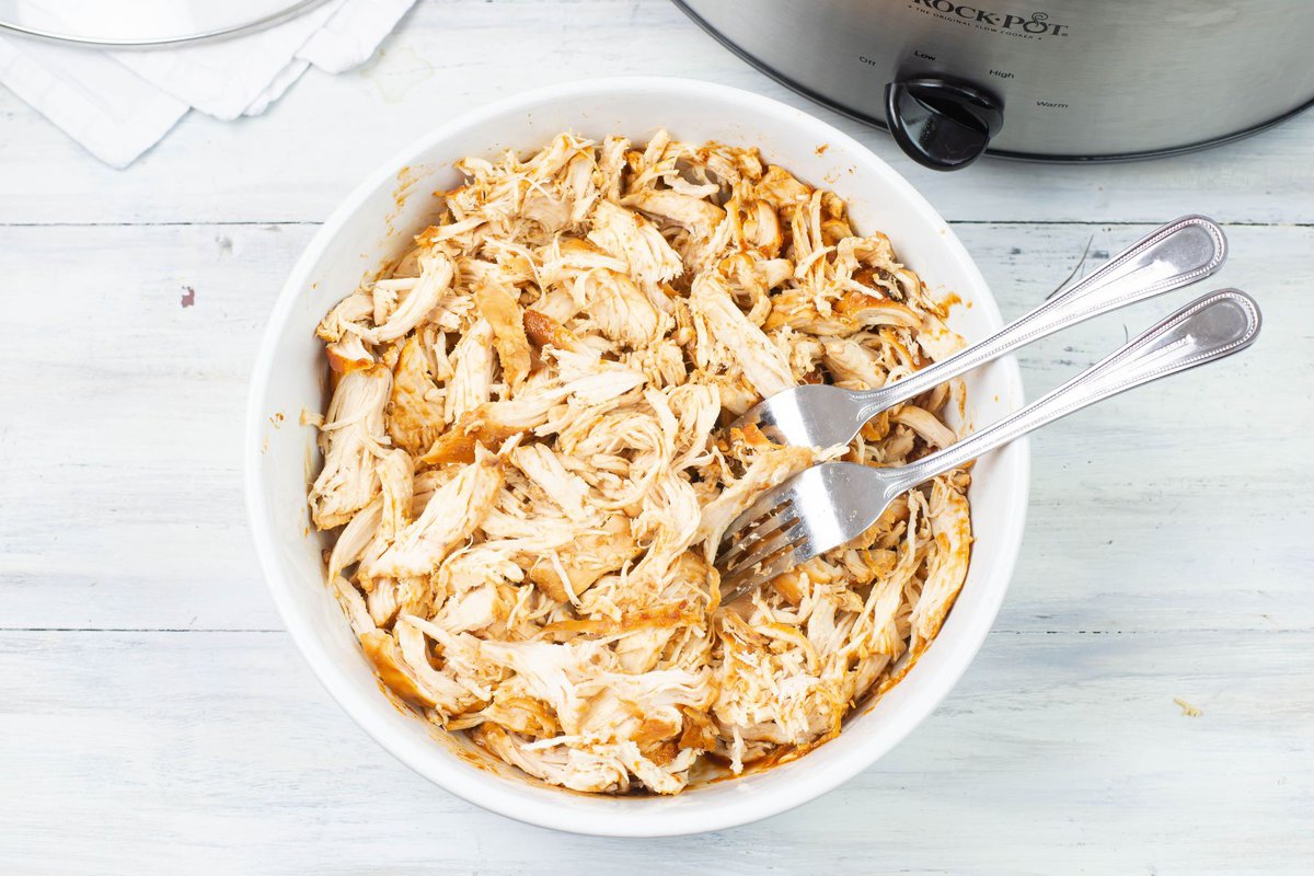 Slow cooked and shredded chicken in a white glass bowl.
