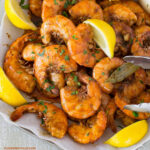 New Orleans Style BBQ Shrimp piled on a serving platter with lemon wedges