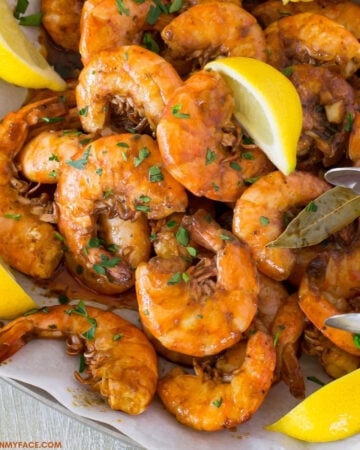 New Orleans Style BBQ Shrimp piled on a serving platter with lemon wedges