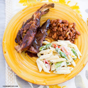 Smoky BBQ Spare ribs served with a side of baked beans and a pasta salad on a yellow glass plate.