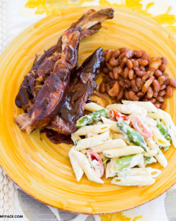 Smoky BBQ Spare ribs served with a side of baked beans and a pasta salad on a yellow glass plate.