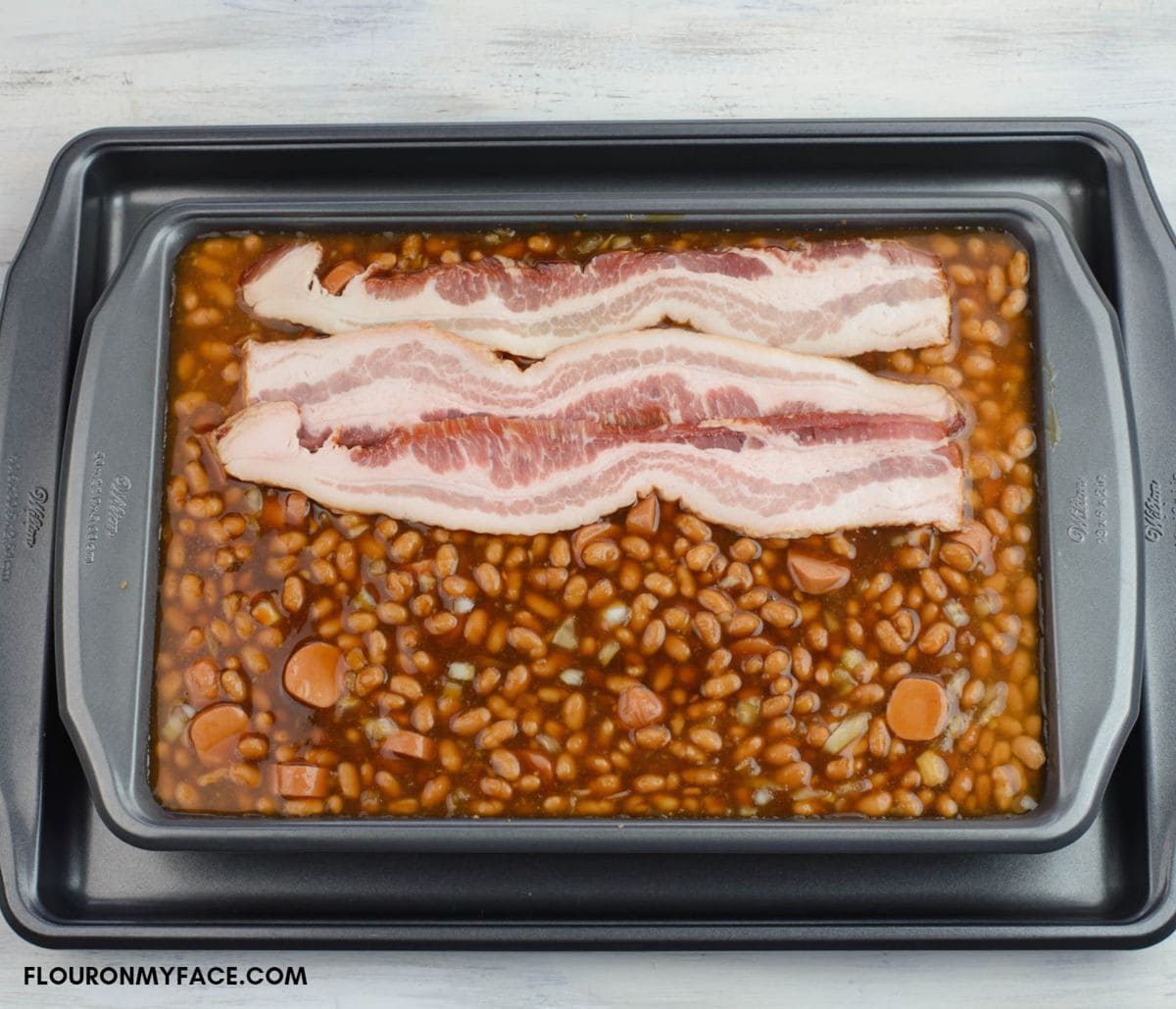 Arranging bacon slices on top of the beans.