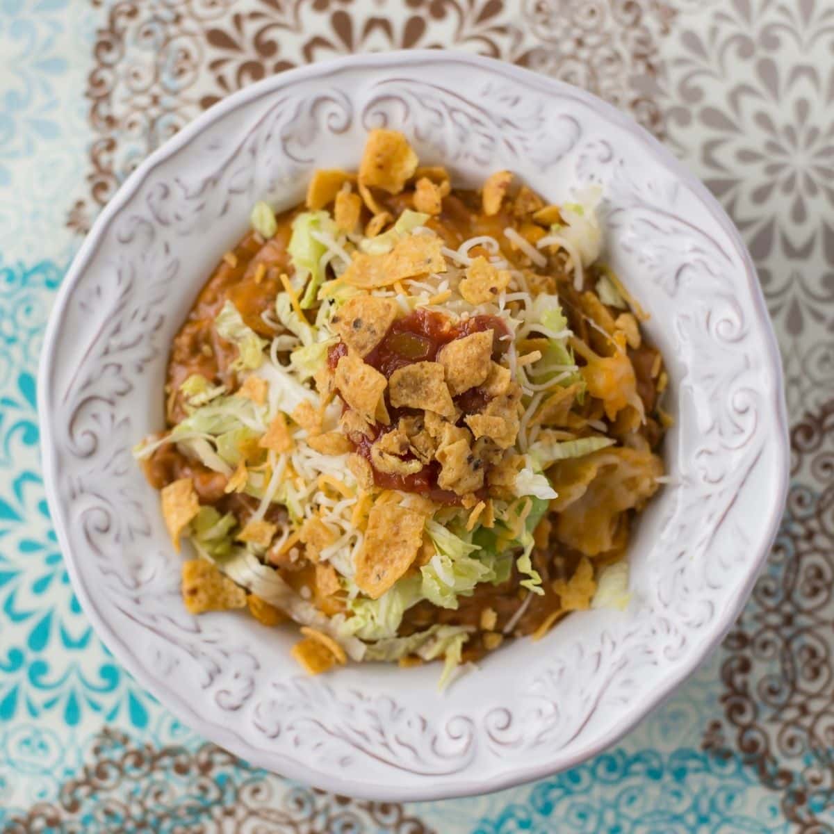 Overhead image of a bowl filled with Frito Taco Casserole topped with lettuce and salsa.