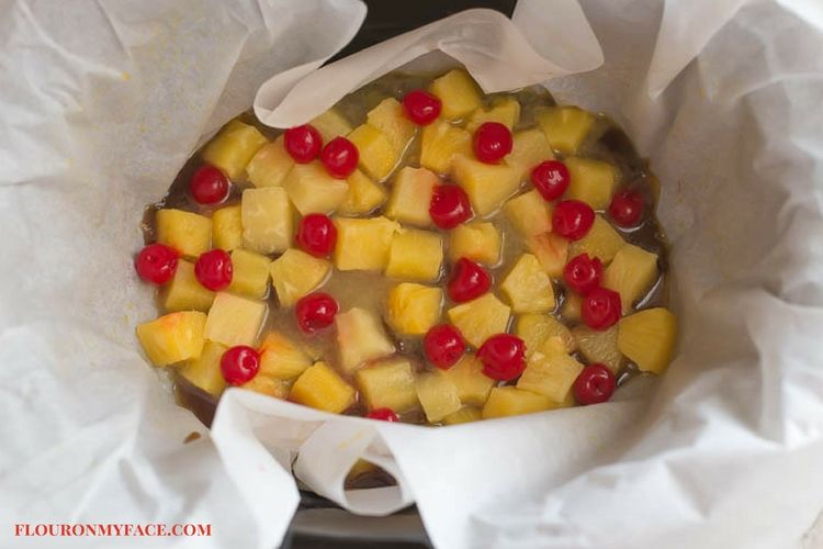 Pineapple Upside Day Cake ingredients in a slow cooker that has been lined with parchment paper for easy removal.
