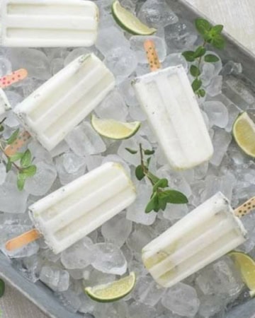 How to serve cocktail popsicles at your next party. Coconut Mojito Ice Pops served in a galvanized steel serving tray on a bed of ice.