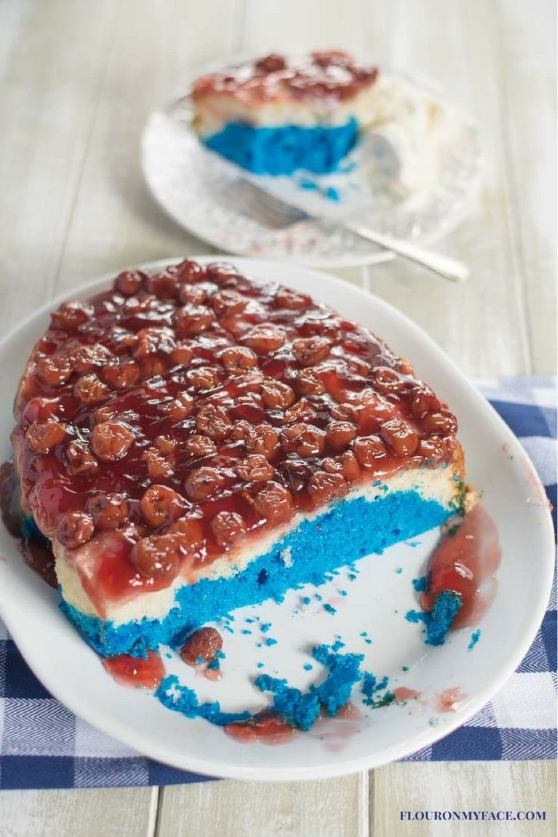 Red, white and blue cake topped with cherry pie filling on a serving platter.