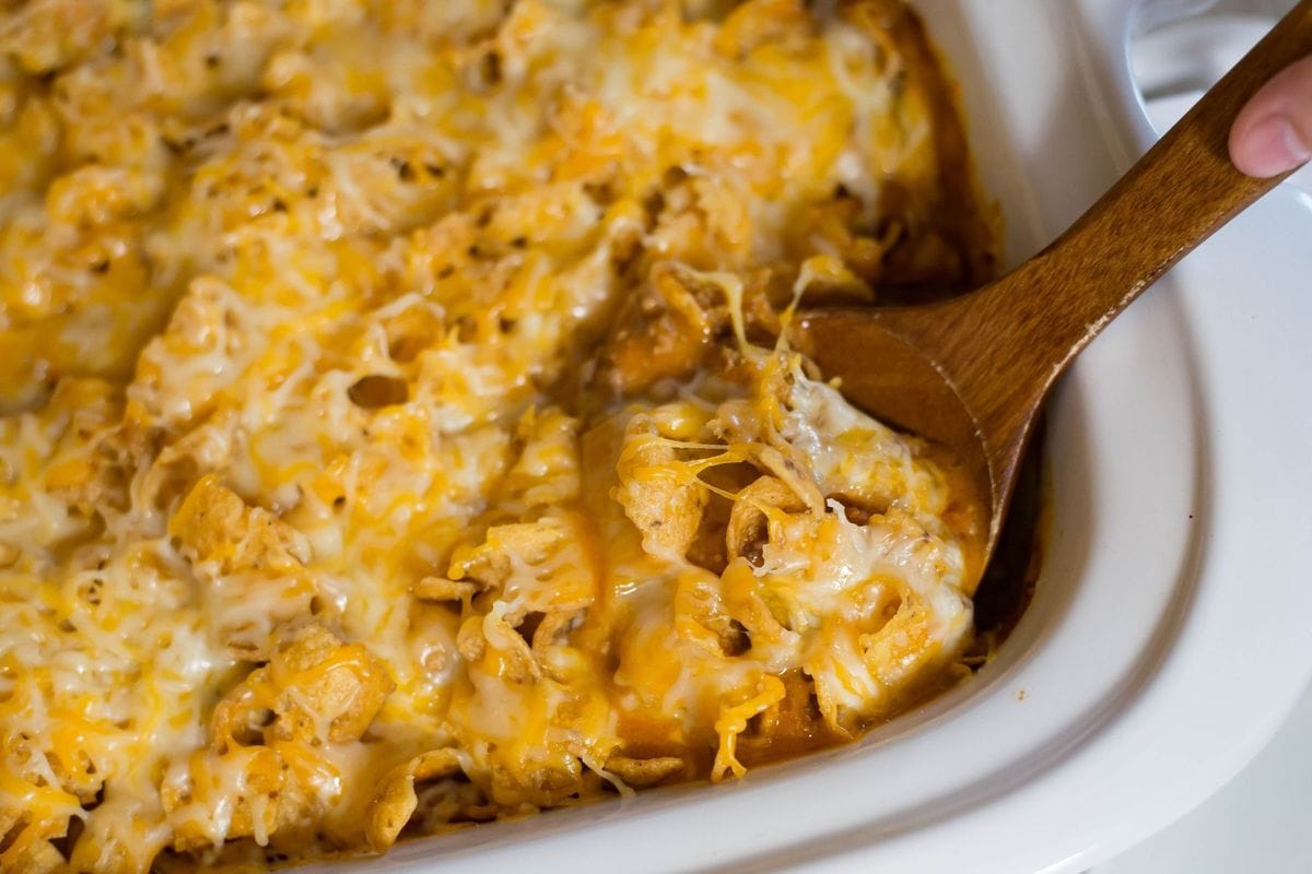 Slow cooker Frito Casserole with a wooden spoon serving a portion.
