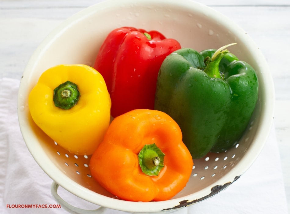 Fresh whole yellow, red, green and orange bell peppers in a white enamel colander