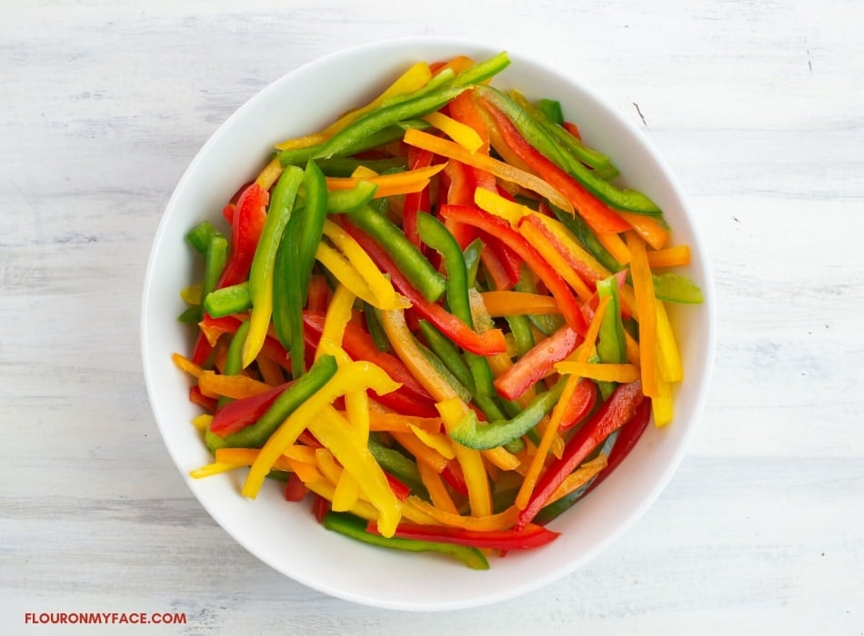 a white glass bowl filled with sliced, red, yellow, orange, and green peppers