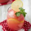 Watermelon lemonade in a tumbler with a garnish of sliced lemon and mint leaves.