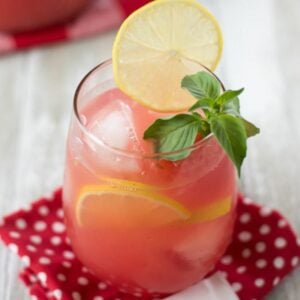 Watermelon lemonade in a tumbler with a garnish of sliced lemon and mint leaves.