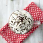 Sweet and Creamy Slow Cooker Hot Cocoa recipe served in a mug, topped with whipped cream and sprinkles on a red cloth napkin