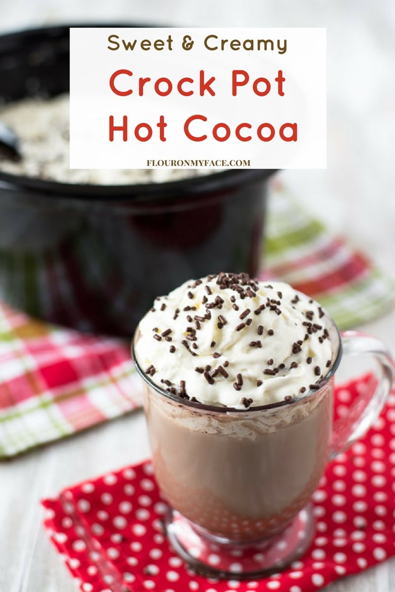 Coffee mug filled with a Crock Pot Hot Cocoa recipe topped with whipped cream and brown sprinkles.