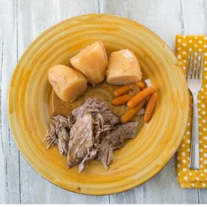 A yellow glass dinner plate with slices pot roast, carrots and potatoes.