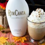 Pumpkin RumChata Latte served in a big clear mug, topped with whipped cream, ground cinnamon and garnished with a cinnamon stick.