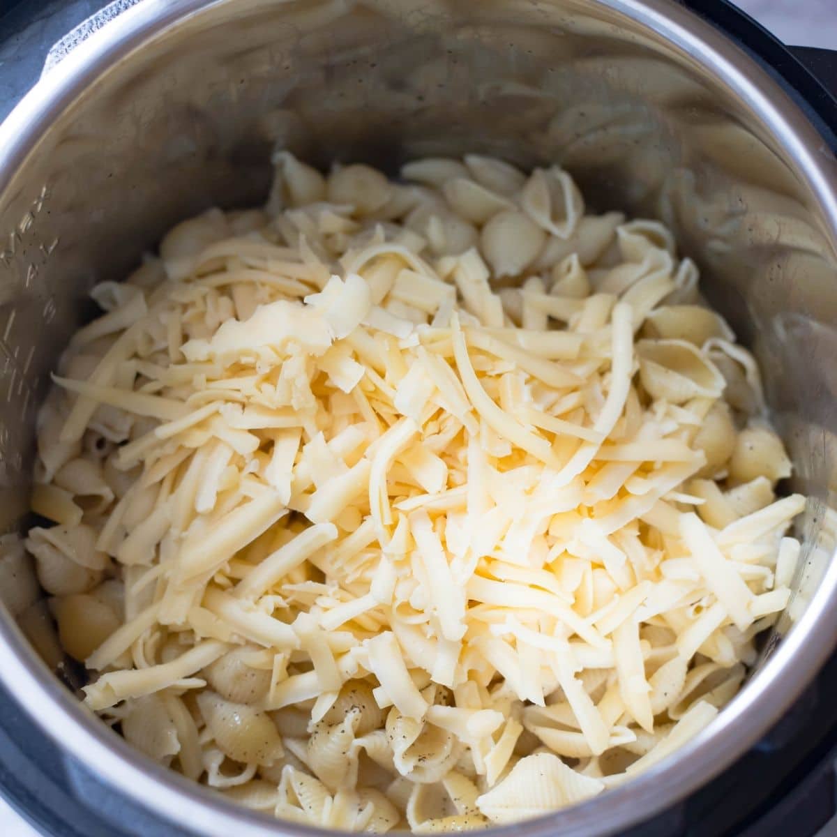 adding shredded gouda cheese to the cooked macaroni.