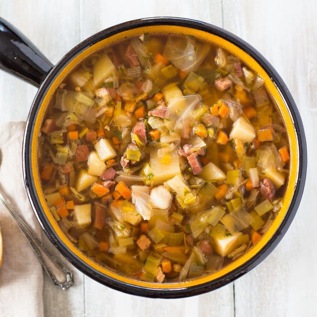 A large brown soup serving bowl filled with Ham Cabbage Potatoes Soup