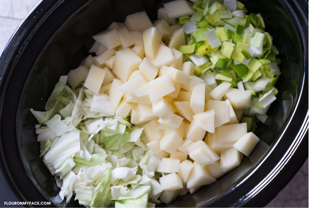 Chopped cabbage, diced potatoes and chopped fennel inside an 8 quart crock pot before cooking