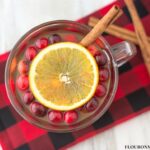 Hot Apple Cider Christmas Wassail recipe served in a mug on a black and red plaid cloth napkin with fresh cranberries, an orange slice and a cinnamon stick for garnish.