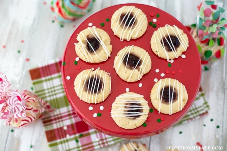 Christmas Jam Thumbprint cookies displayed on a red cake pedestal on top of a red, green and white cloth napkin. 