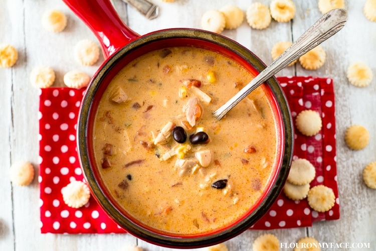 Slow Cooker Chicken Santa Fe Soup recipe served in a red soup bowl on a red cloth napkin with vintage silverware spoons