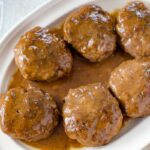 Salisbury Steak comfort food recipe. Cooked Salisbury Steak patties covered in gravy served on a off white serving platter.