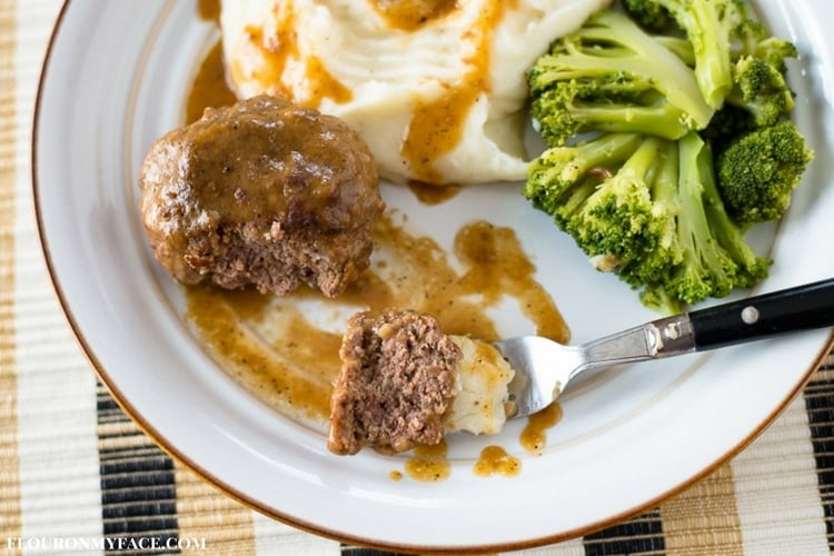a serving of Crock Pot Salisbury Steak served with mashed potatoes, gravy and fresh steamed broccoli on a white dinner plate. 