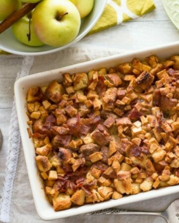 Mother's Day Apple Cinnamon Bacon Breakfast Casserole on table with plates, vintage silverware and a bowl of yellow apples