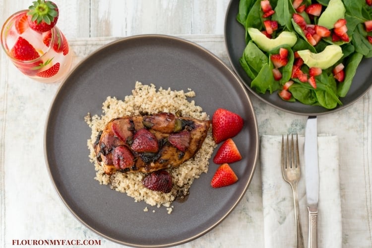 Plate of roasted Strawberry Balsamic Chicken with quinoa and a strawberry spinach salad served on charcoal dinner plates.