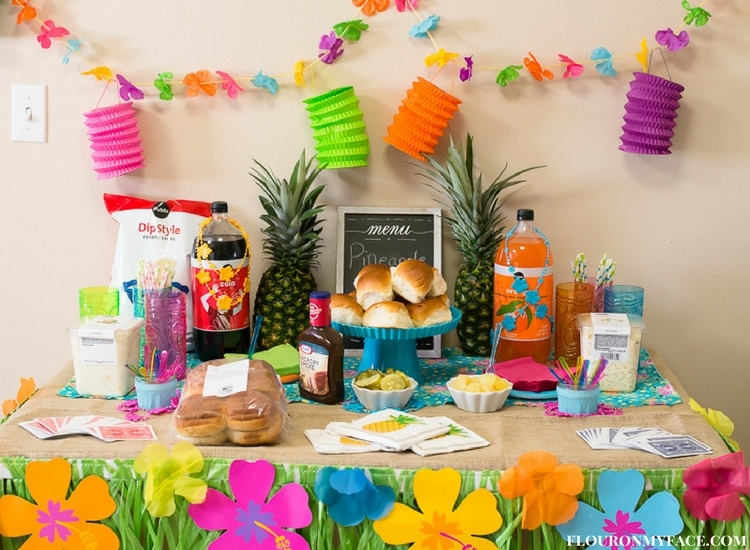 Luau Game Night Table top decorated with a grass banner and Luau themed food. Pineapple Pulled Pork Sliders and supplies from Publix