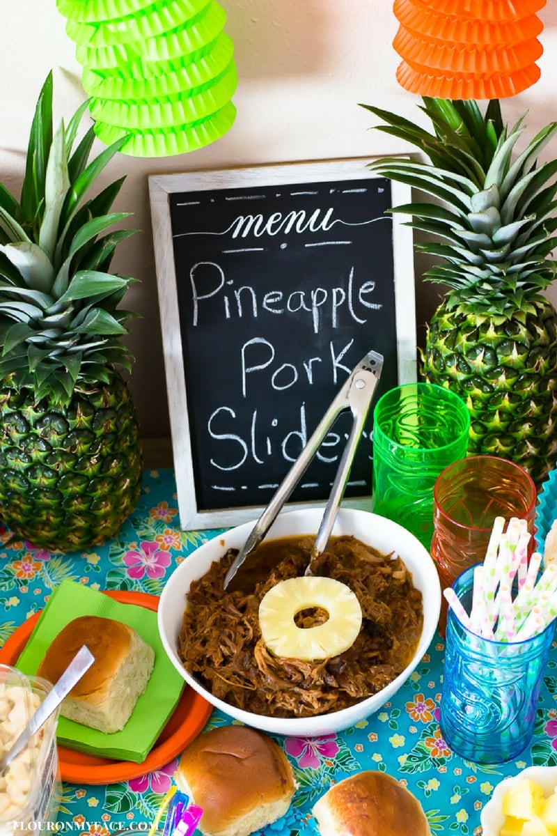 Crock Pot Pulled Pork recipe in a white serving bowl on a Luau themed party table with fresh pineapple in the background