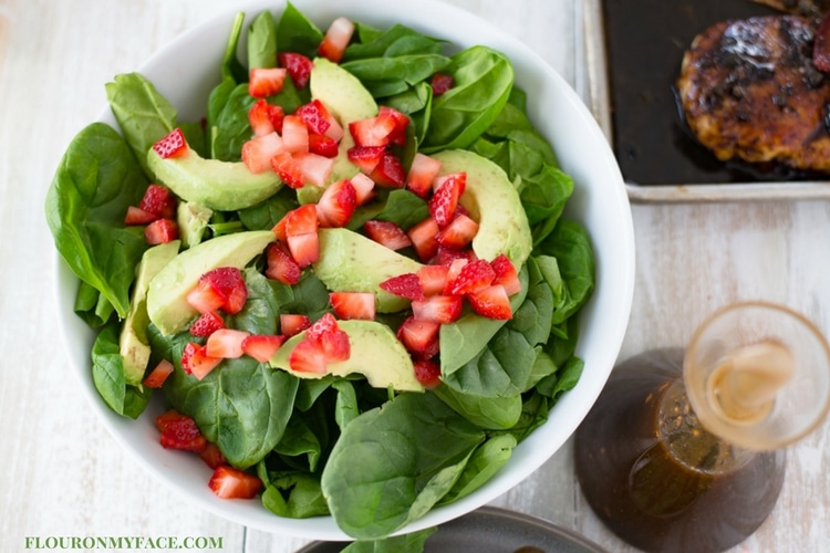 A bowl of spinach, strawberry and avocado salad served with a bottle of homemade Balsamic Vinaigrette Dressing