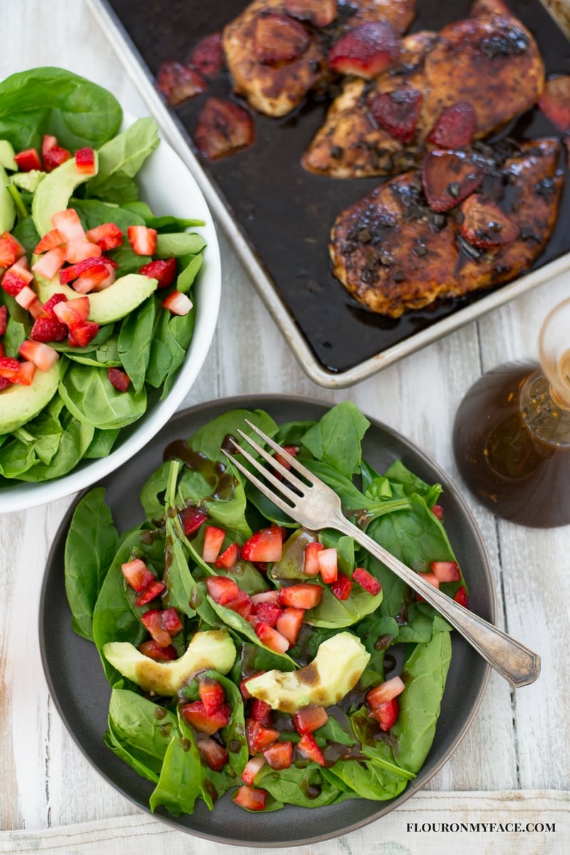 Spinach Strawberry Avocado Salad recipe with Balsamic Vinaigrette served on a charcoal black plate with a baking pan of Strawberry Balsamic Chicken