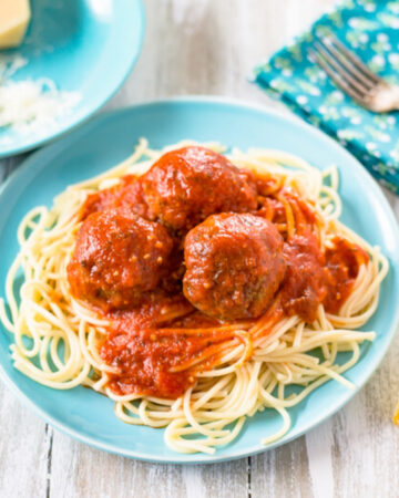 A light blue plate with a serving of cooked spaghetti noodles with 3 meatballs with spaghetti sauce on top of the pasta