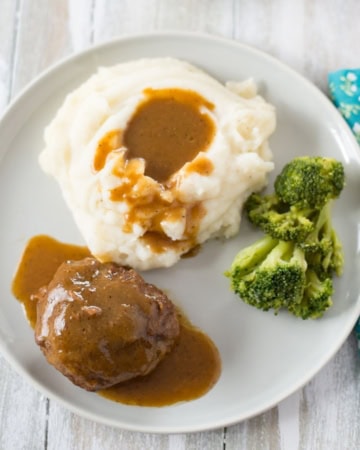 Dinner plate with a serving of Salisbury Steak, mashed potatoes, and fresh broccoli.