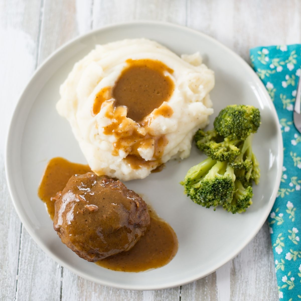 Dinner plate with a serving of Salisbury Steak, mashed potatoes, and fresh broccoli.