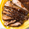 A yellow glass serving platter with a slow cooker smoked barbecue beef brisket that has been sliced for serving
