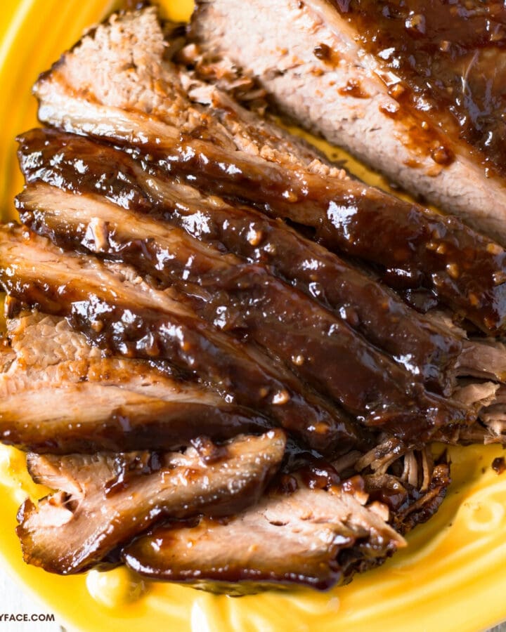 A yellow glass serving platter with a slow cooker smoked barbecue beef brisket that has been sliced for serving