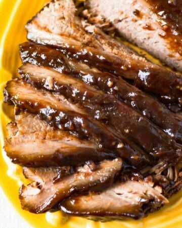 A yellow glass serving platter with a slow cooker smoked barbecue beef brisket that has been sliced for serving