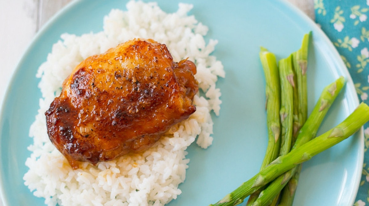 Crock Pot Honey Garlic Chicken Thighs served on a bed of cooked white rice with fresh asparagus