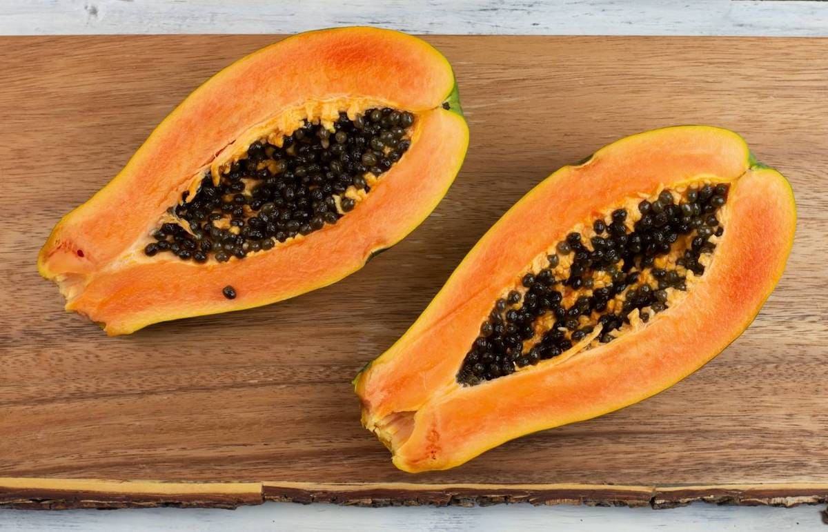 A fresh papaya cut open in half on a wooden cutting board.