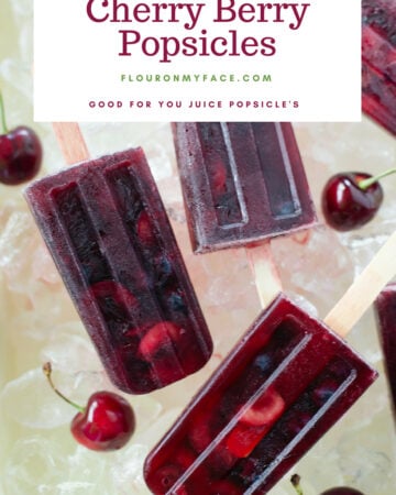 Homemade real fruit juice cherry popsicles with sliced cherries and fresh blueberries served in a vintage enamel baking pan on ice cubes.