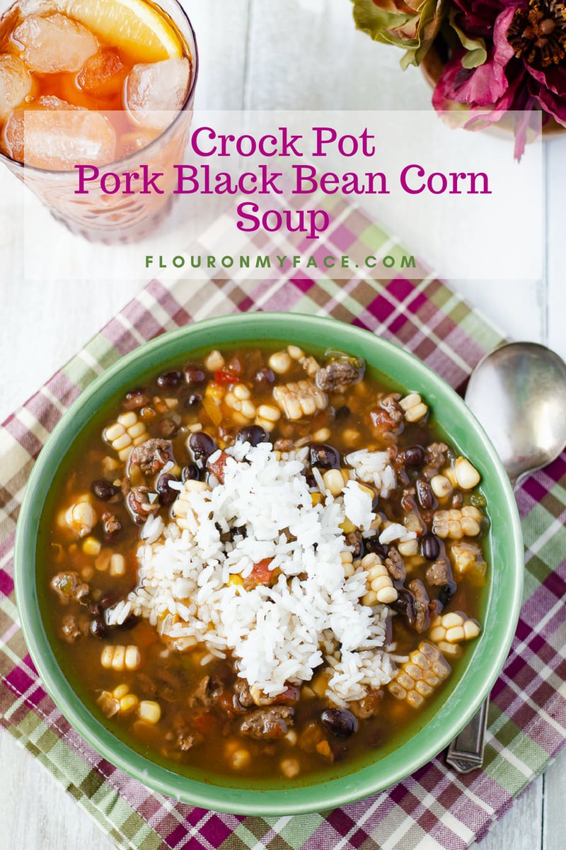 A green bowl with a serving of Crock Pot Pork Black Bean Corn soup using leftover corn on the cob with a glass of sweet iced tea.
