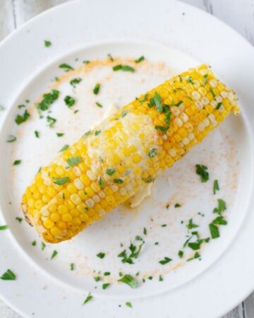 An ear of Instant Pot corn on the cob on a white plate, melted butter and parsley.